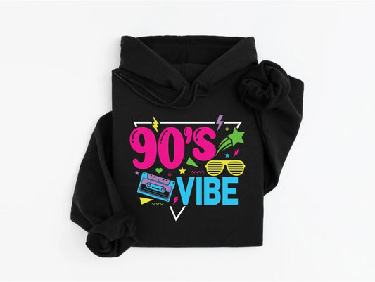 A black hoodie featuring a vibrant retro design with the text “90’s Vibe.” The graphic includes neon-colored illustrations of a cassette tape, sunglasses, stars, lightning bolts, and other fun 90’s-inspired elements